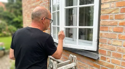 Malermester maler hvidt trævindue på murstenshus fra stige