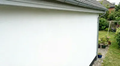 Nymalet hvid husfacade med tagrender og have i baggrunden