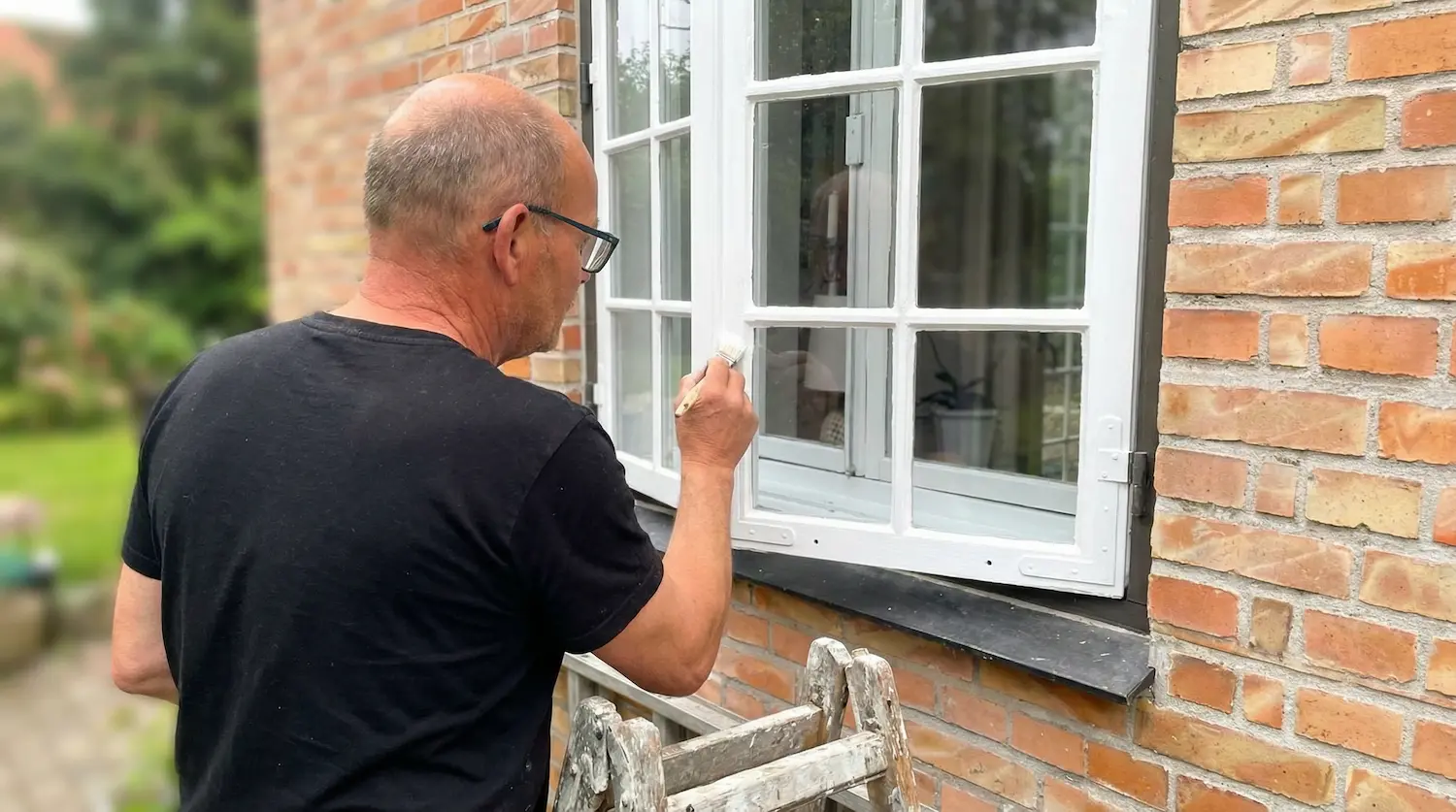 Malermester Leon Meyer maler hvidt trævindue på murstenshus fra stige