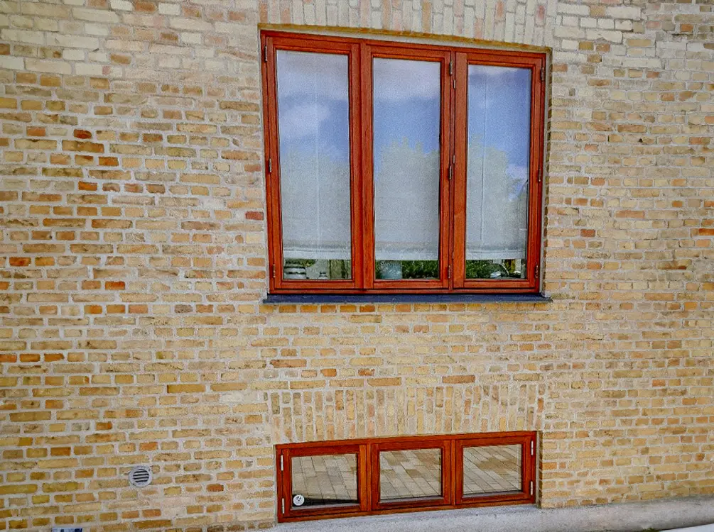 Røde trævindueskarme mod gul mursten, udvendigt træværk klar til maling